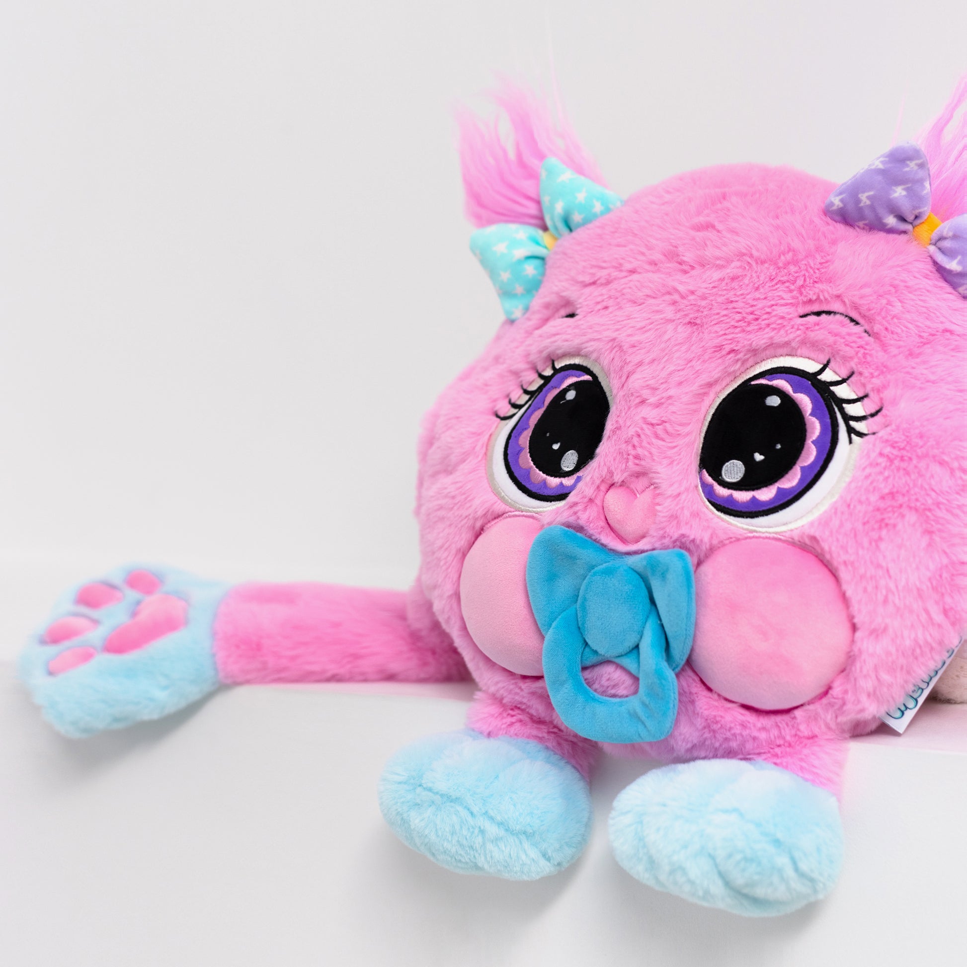 A pink and blue plush weighted toy featuring 3D sensory cheeks, paws, and nose, with large eyes set against a white background.